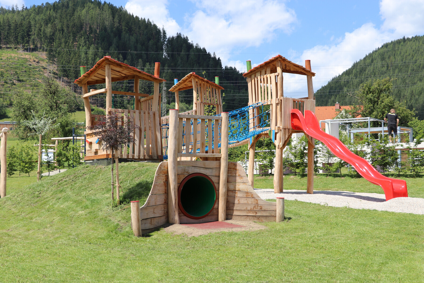 Holzspielanlage mit Türmen, Tunnel und roter Rutsche