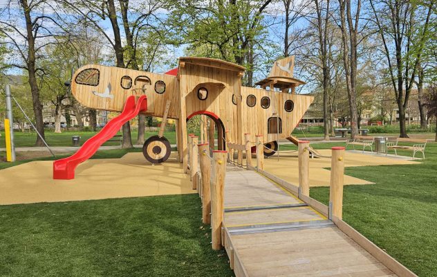 Holzspielanlage in Flugzeugform mit Zugangsweg und roter Rutsche